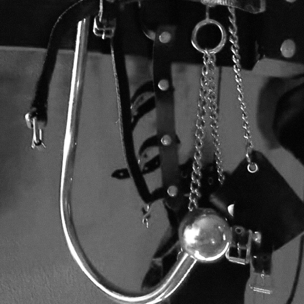 Black and white close-up of BDSM metal restraints and chains hanging on a rack