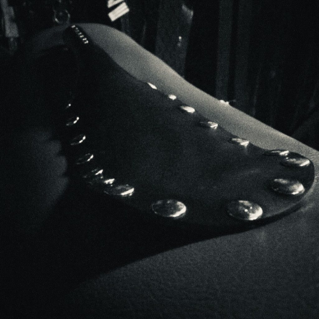 Black and white close-up of a leather paddle with metal studs on a textured surface
