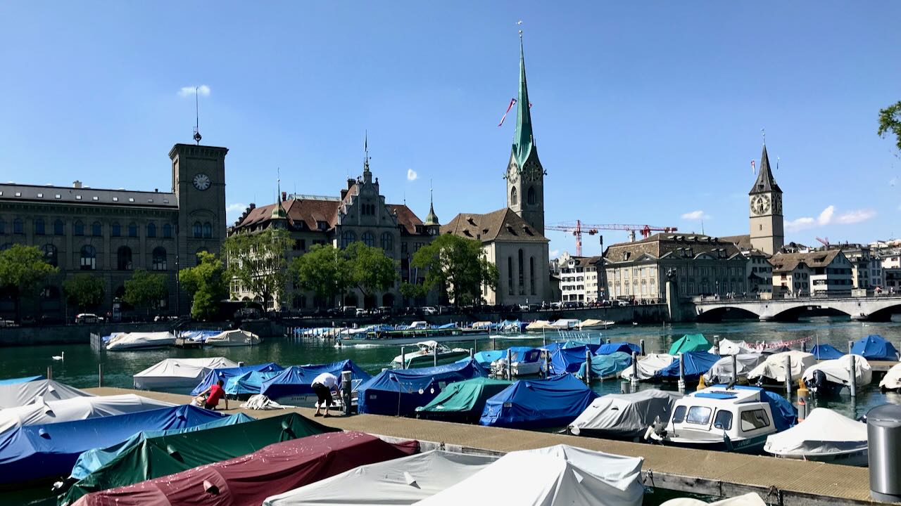 Zürich mit Blick auf die Limmat, Bootsanleger und markante Kirchtürme der Altstadt.