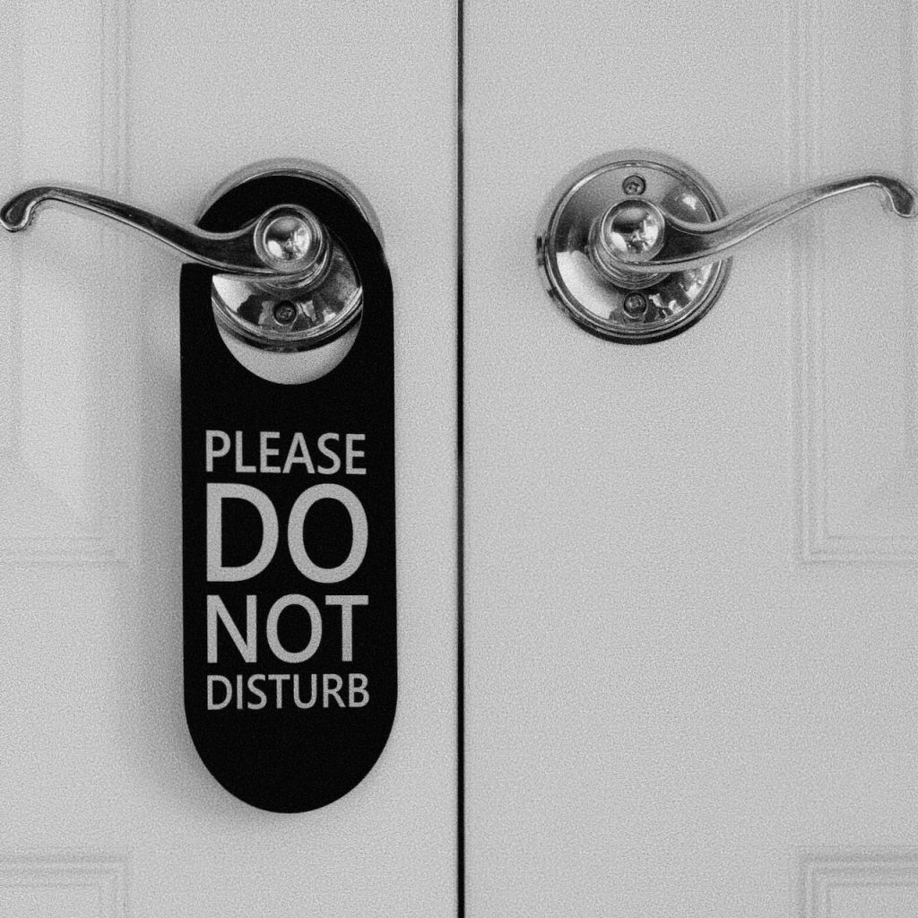 Black and white close-up of a door handle with a “Please Do Not Disturb” sign hanging from it.